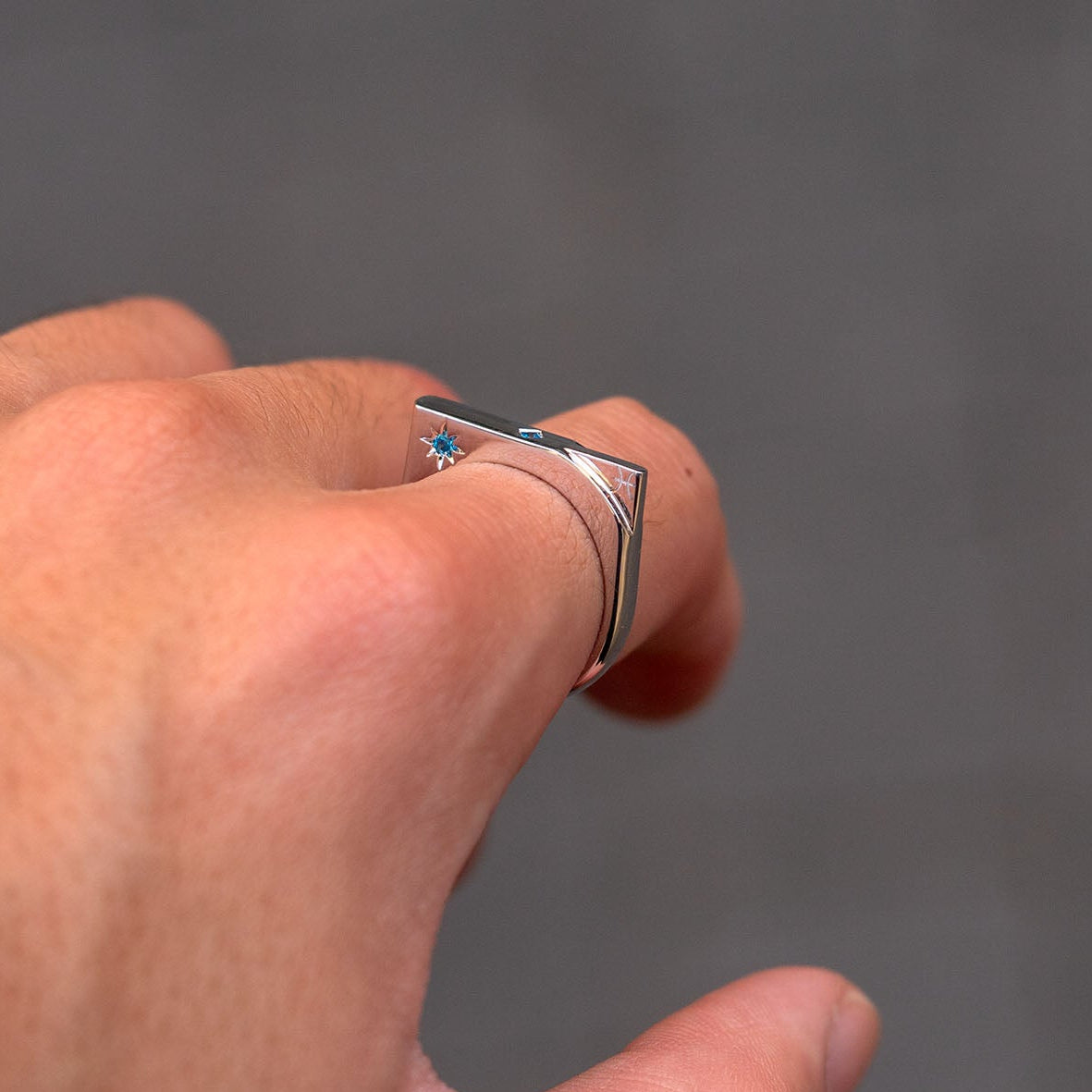 Hand wearing a silver ring with a blue gemstone on a gray background